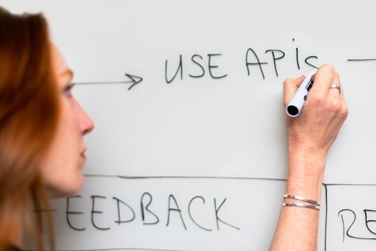 A woman writes Use APIs on a whiteboard, focusing on software planning and strategy.